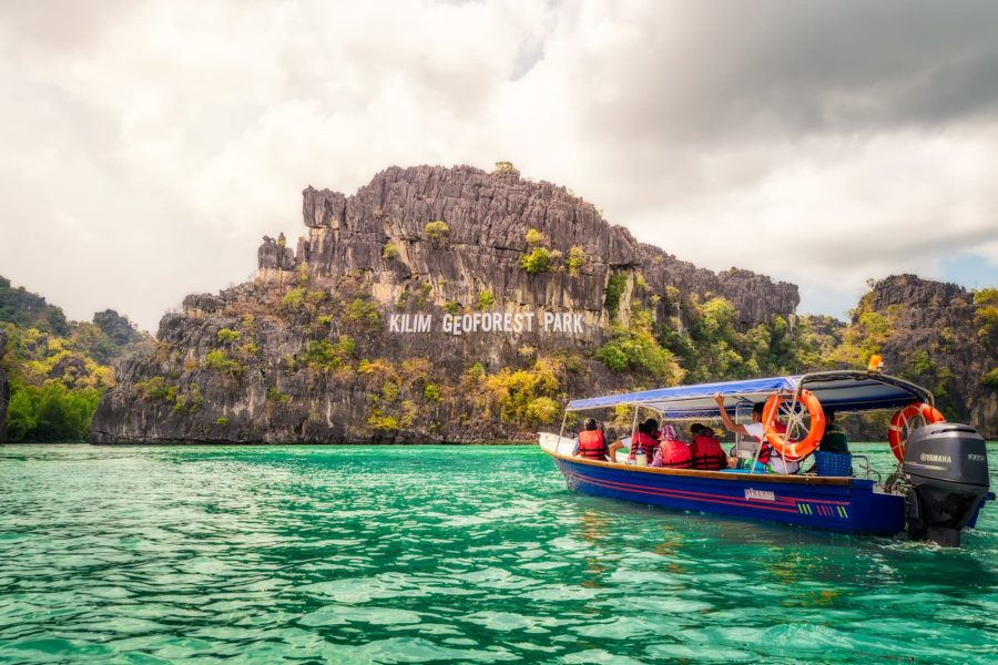 A boat passing beneath the Kilim Geoforest Park limestone cliffs